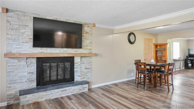 dining area with wood finished floors, a fireplace, a textured ceiling, baseboards, and ornamental molding