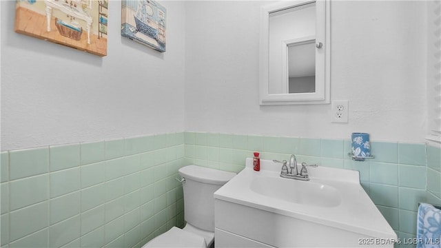 bathroom with toilet, tile walls, vanity, and wainscoting