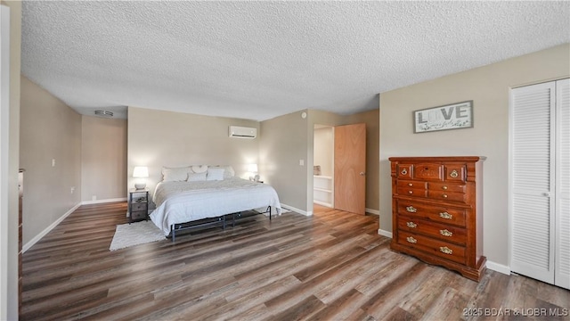 bedroom with baseboards, a wall mounted air conditioner, a textured ceiling, and wood finished floors