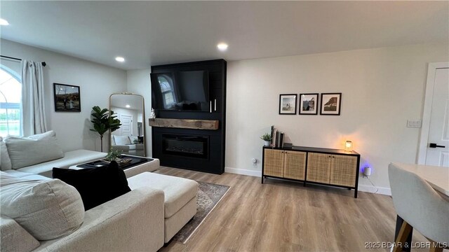 living area featuring wood finished floors, a large fireplace, recessed lighting, and baseboards
