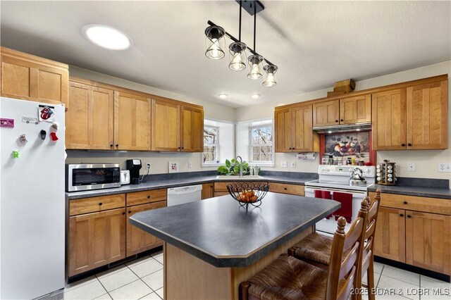 kitchen with dark countertops, a breakfast bar, white appliances, a sink, and light tile patterned floors