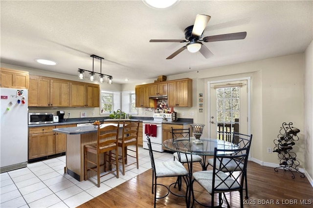 kitchen featuring ceiling fan, a kitchen island, a kitchen bar, dark countertops, and white appliances