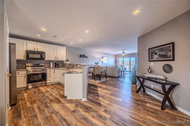 1359 Seascape Ln Unit A-501, Osage Beach, MO 65065 - kitchen with appliances with stainless steel finishes, a peninsula, dark wood-type flooring, decorative backsplash, and white cabinetry