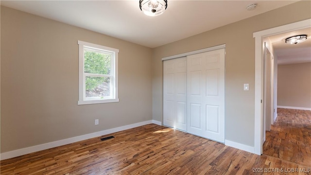 unfurnished bedroom featuring baseboards, wood finished floors, and a closet