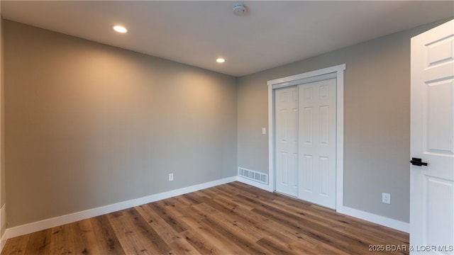 unfurnished bedroom with baseboards, wood finished floors, recessed lighting, and a closet