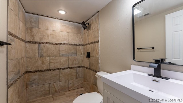 bathroom featuring toilet, a tile shower, and vanity