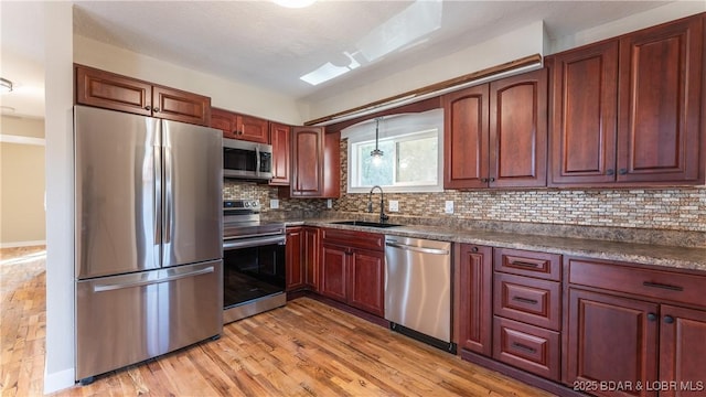 kitchen with appliances with stainless steel finishes, a sink, dark countertops, and tasteful backsplash