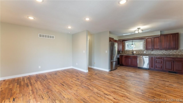 kitchen featuring stainless steel appliances, a sink, light wood-style flooring, baseboards, and decorative backsplash