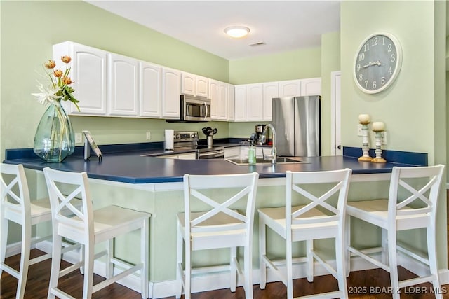 kitchen with appliances with stainless steel finishes, a sink, dark countertops, and a peninsula