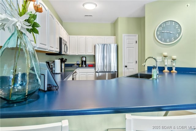 kitchen featuring stainless steel appliances, a sink, white cabinetry, dark countertops, and a peninsula