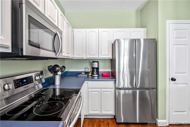 kitchen with stainless steel appliances, white cabinets, dark countertops, and dark wood-style flooring