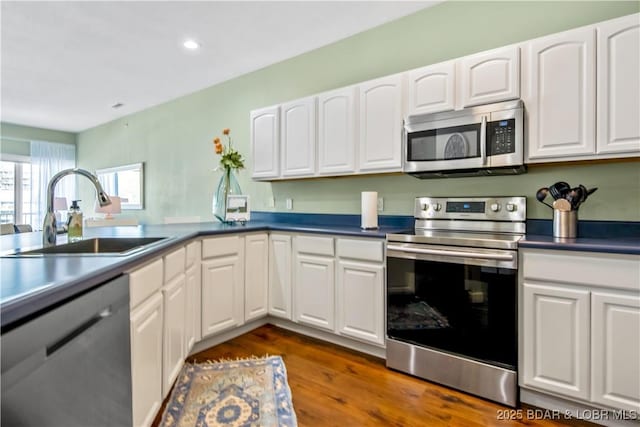 kitchen with appliances with stainless steel finishes, a sink, white cabinetry, dark wood finished floors, and recessed lighting