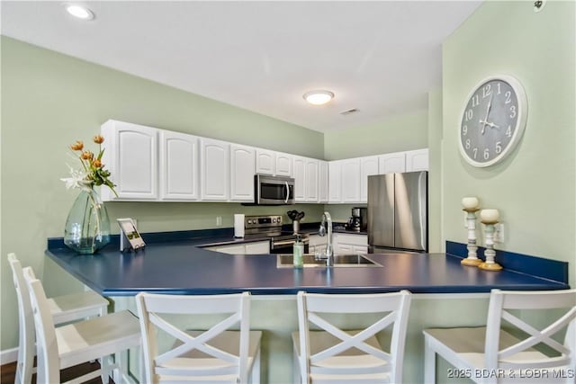 kitchen with appliances with stainless steel finishes, dark countertops, a peninsula, white cabinets, and a sink