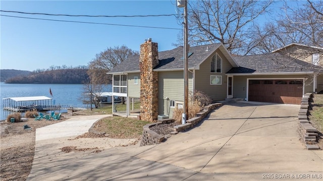 view of front facade with a chimney, an attached garage, driveway, and a water view