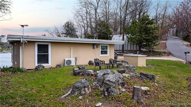 back of house at dusk featuring concrete block siding, a lawn, and ac unit