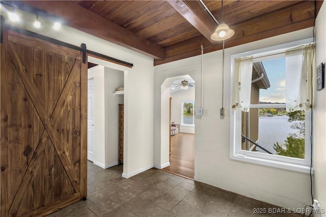 hall featuring a barn door, wooden ceiling, beamed ceiling, baseboards, and dark tile patterned flooring