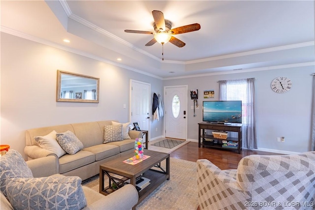 living area with a tray ceiling, baseboards, a ceiling fan, wood finished floors, and ornamental molding
