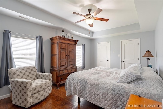 bedroom featuring baseboards, visible vents, ceiling fan, dark wood-type flooring, and a raised ceiling