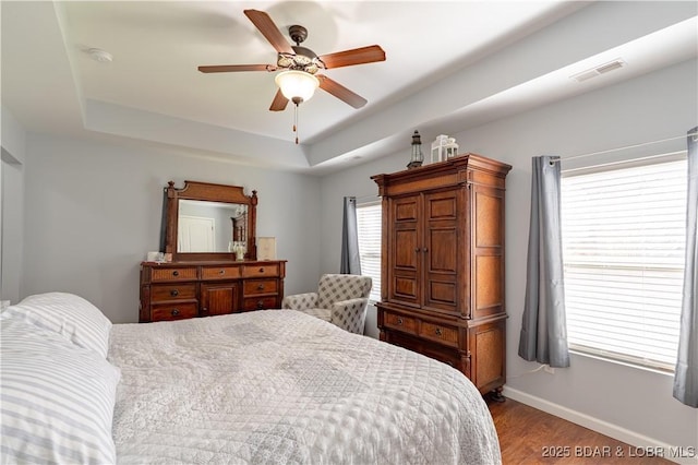bedroom featuring baseboards, visible vents, wood finished floors, ceiling fan, and a raised ceiling