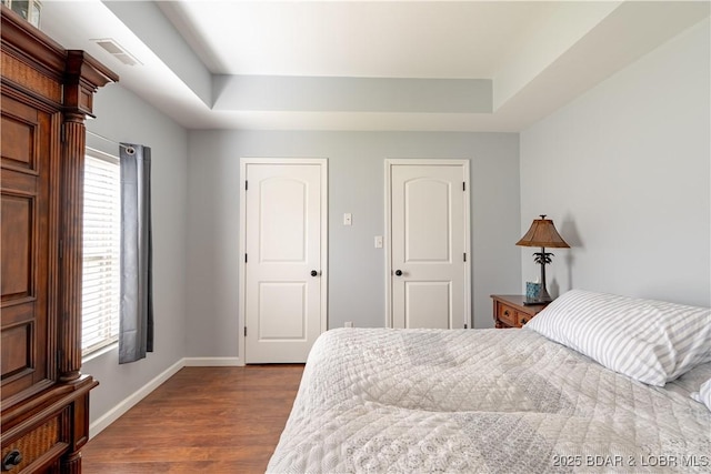 bedroom with dark wood finished floors, multiple windows, a tray ceiling, and visible vents