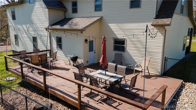 rear view of house featuring outdoor dining space, roof with shingles, and a deck