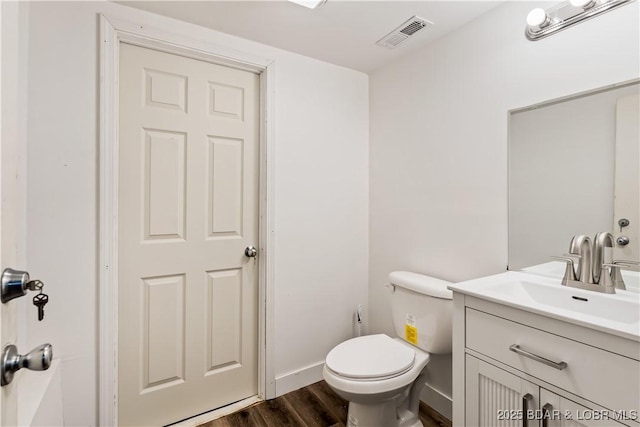 half bathroom featuring toilet, visible vents, baseboards, wood finished floors, and vanity