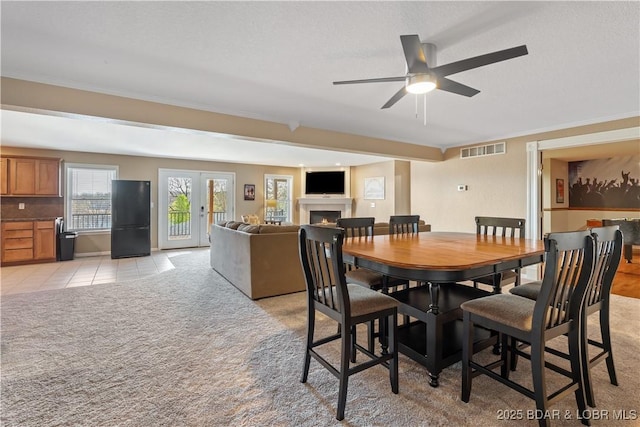 dining area featuring a warm lit fireplace, light tile patterned floors, ceiling fan, light colored carpet, and visible vents