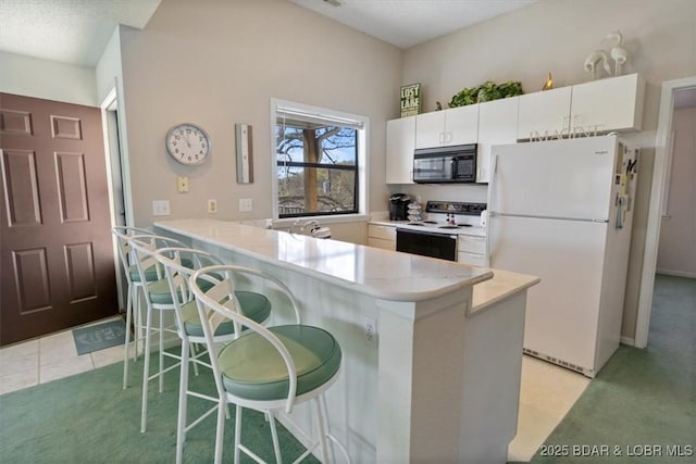 kitchen featuring white appliances, a breakfast bar area, light colored carpet, white cabinets, and a peninsula
