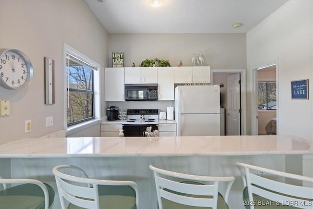 kitchen with black microwave, electric range, a peninsula, white cabinetry, and freestanding refrigerator