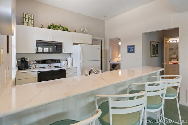 kitchen featuring freestanding refrigerator, black microwave, a kitchen bar, electric range, and white cabinetry