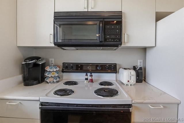 kitchen featuring black microwave, light countertops, white cabinetry, and electric stove