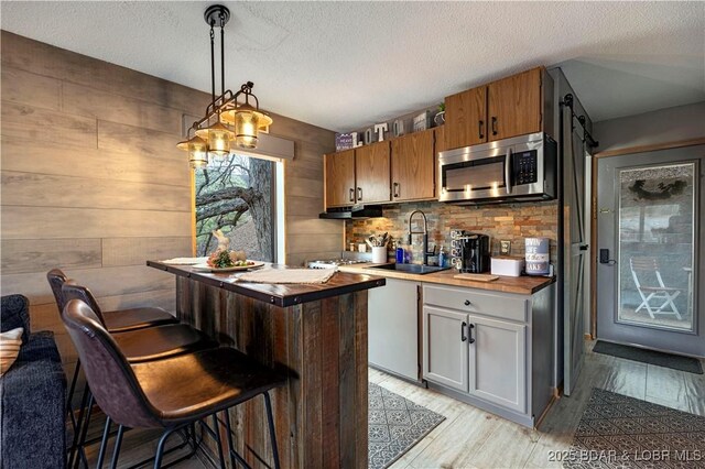 bar with light wood finished floors, a sink, stainless steel microwave, tasteful backsplash, and a textured ceiling