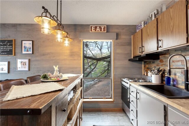 kitchen with under cabinet range hood, light countertops, stainless steel range with gas stovetop, a sink, and a textured ceiling