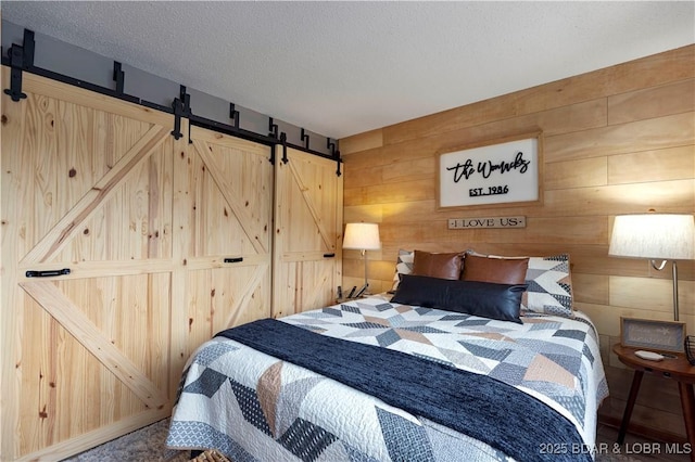bedroom with a barn door, wood walls, and a textured ceiling
