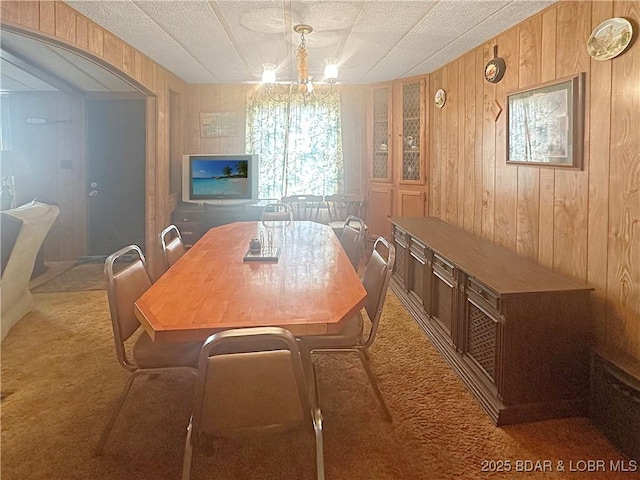 796 1051st Rd SE, Mo, MO 64740 - carpeted dining room with arched walkways, a textured ceiling, wood walls, and an inviting chandelier