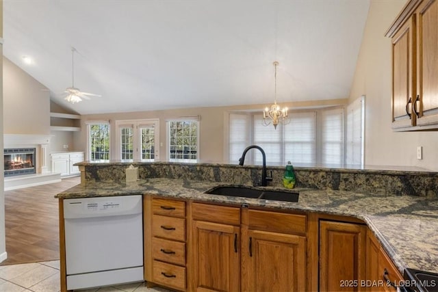 kitchen featuring white dishwasher, a sink, ceiling fan, brown cabinets, and a glass covered fireplace