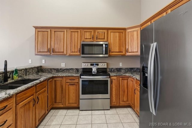 kitchen featuring stainless steel appliances, a sink, brown cabinetry, and light tile patterned floors