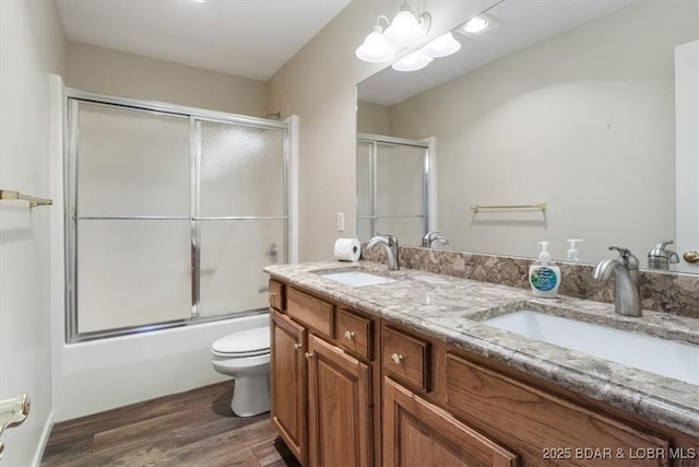 full bath with wood finished floors, double vanity, enclosed tub / shower combo, and toilet