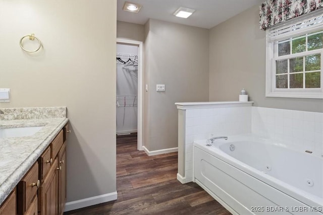 full bathroom featuring baseboards, wood finished floors, vanity, a tub with jets, and a walk in closet