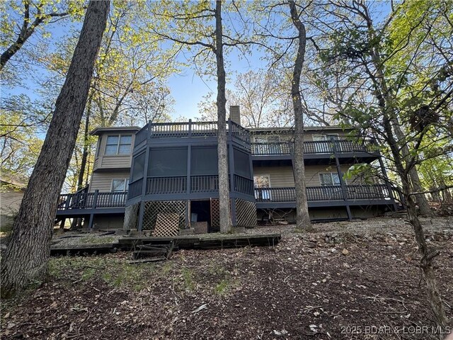 rear view of house with a deck, a chimney, and a sunroom