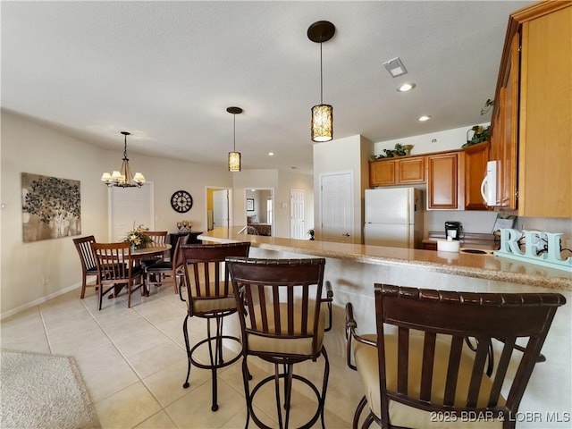 kitchen with hanging light fixtures, white appliances, a kitchen breakfast bar, brown cabinetry, and a peninsula