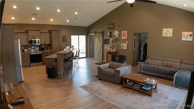 living room featuring light wood-type flooring, a ceiling fan, recessed lighting, and a barn door