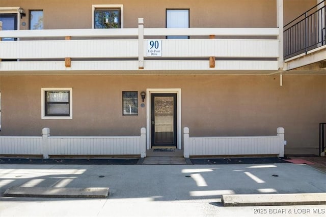 view of exterior entry with a balcony and stucco siding