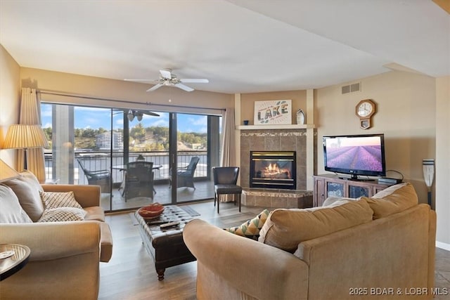 living area with a tile fireplace, visible vents, a ceiling fan, and wood finished floors