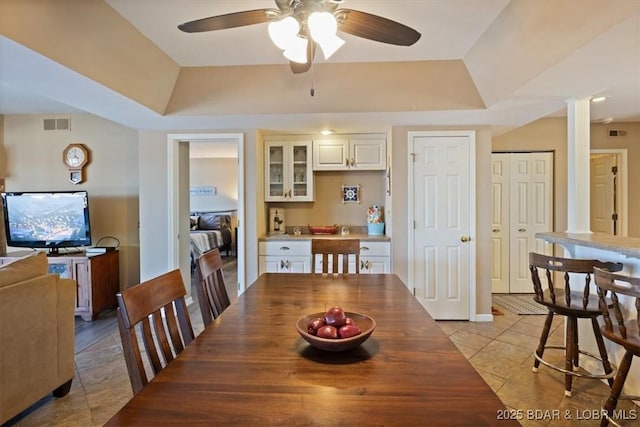 dining room featuring decorative columns, visible vents, a raised ceiling, and a ceiling fan