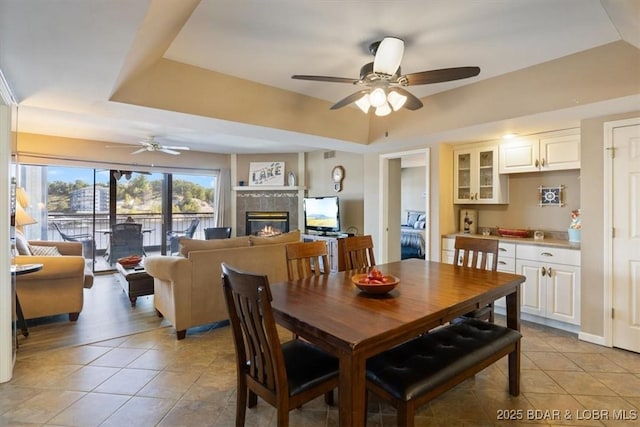 dining room featuring a fireplace, a tray ceiling, a ceiling fan, and light tile patterned floors