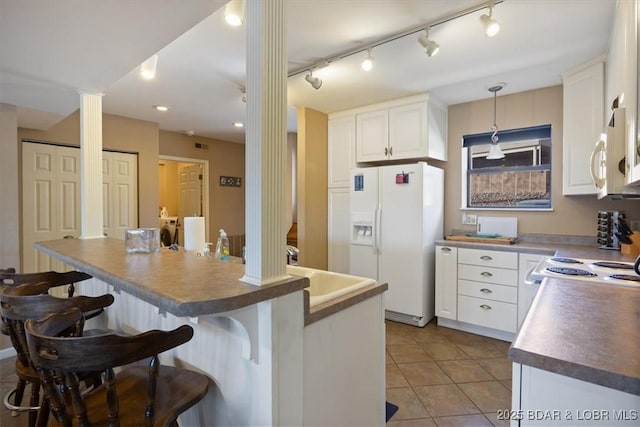 kitchen with a kitchen breakfast bar, white appliances, light tile patterned floors, white cabinetry, and decorative columns