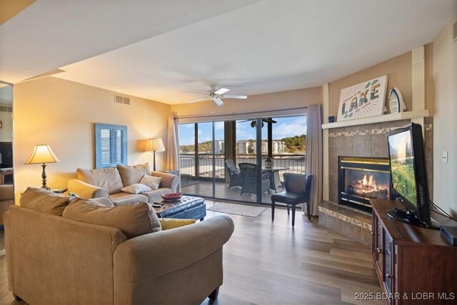 living area featuring a tiled fireplace, wood finished floors, visible vents, and a ceiling fan