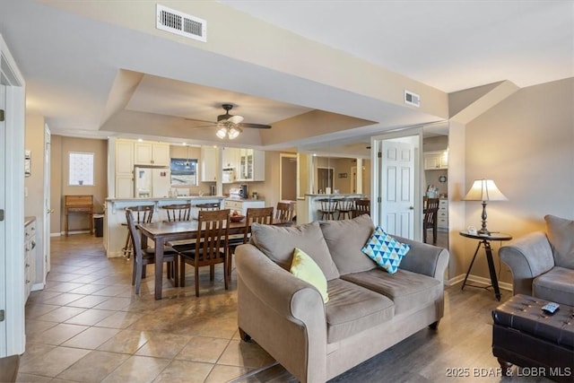 living area featuring ceiling fan, baseboards, visible vents, and a raised ceiling