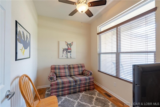 living area with wood finished floors, a ceiling fan, plenty of natural light, and baseboards